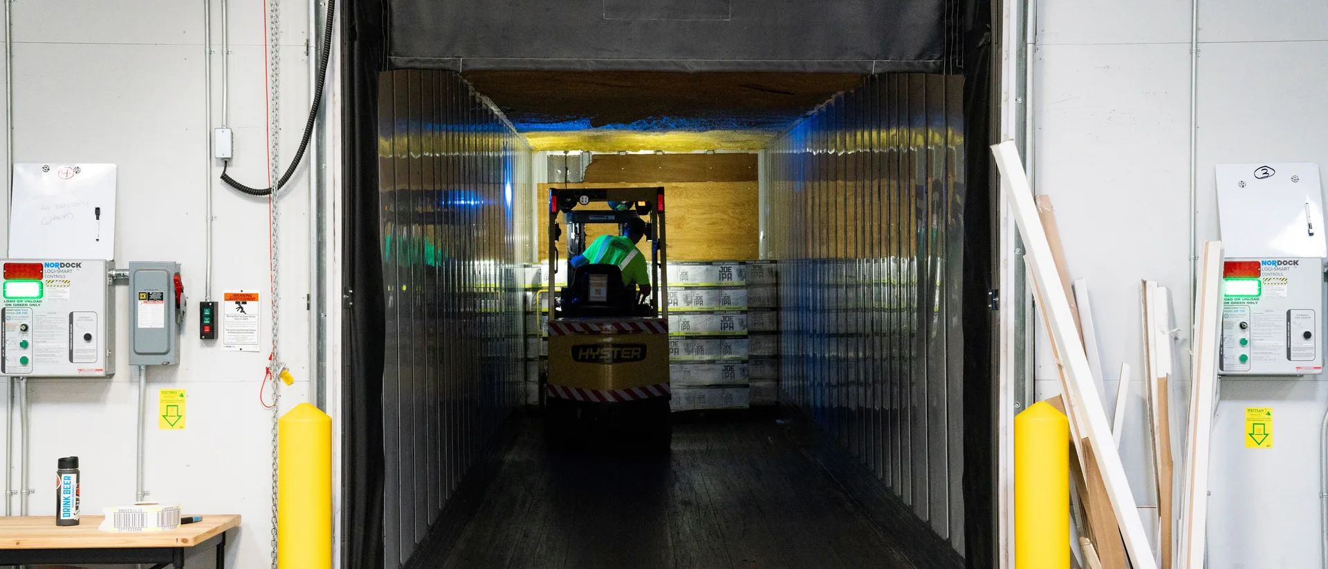 A forklift operator loading palletized freight into a trailer at a warehouse loading dock.