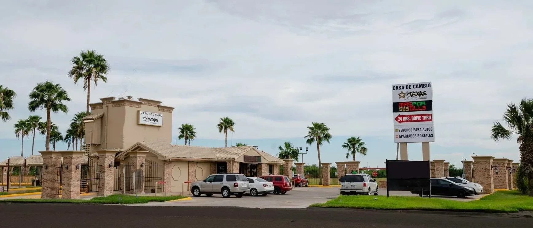 A Texas Money Exchange casa de cambio branch in the Rio Grande Valley, with drive-thru lanes and a roadside sign advertising currency exchange, auto insurance, and postal boxes.